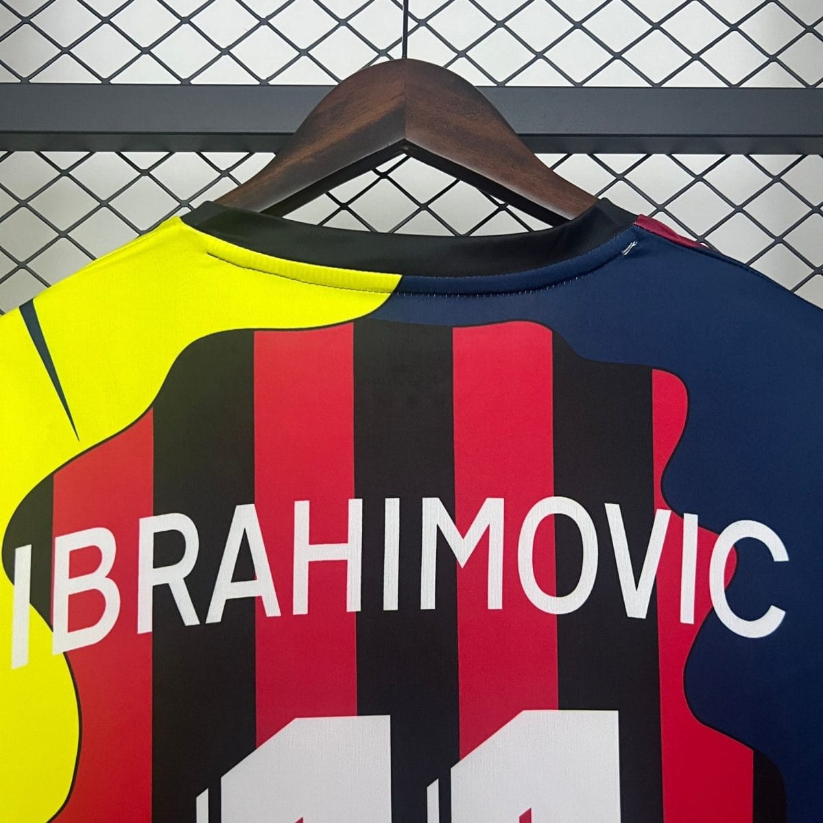 Close-up of a bright neon yellow athletic shirt on a wooden hanger, with bold red/black text, in front of a diamond-pattern metal grid background.