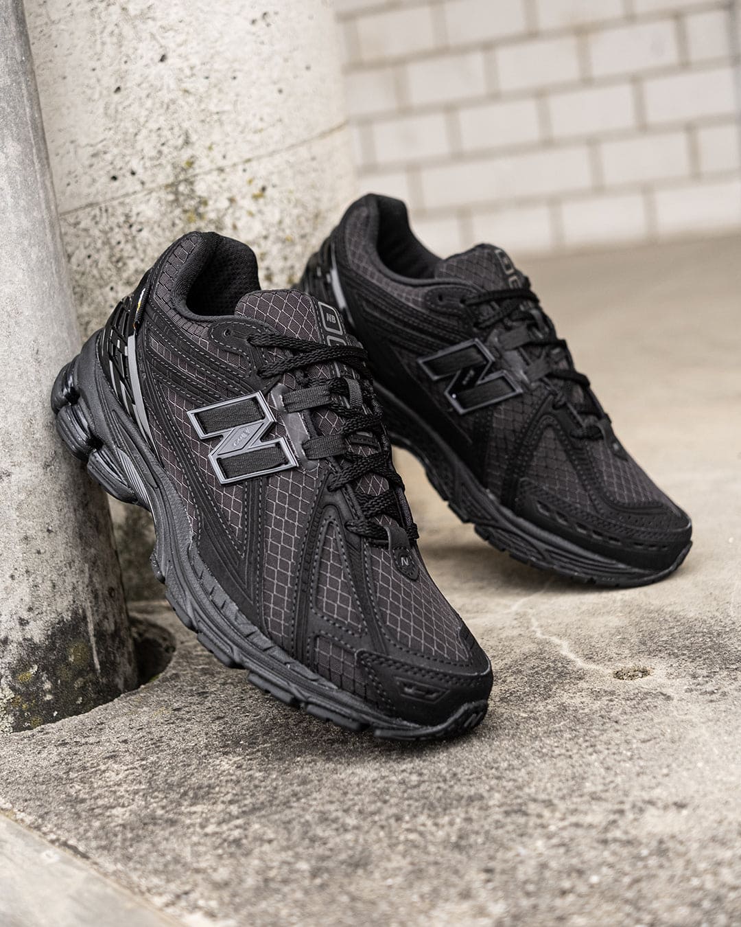 482321426_938859945085191_4832454902399435489_n | UAE SPORT STORE Pair of black running sneakers with a chunky sole leaning against a concrete column outdoors.
