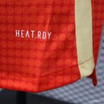 Close-up of red backpack fabric with white 'HEAT.RDY' branding and a beige side panel.