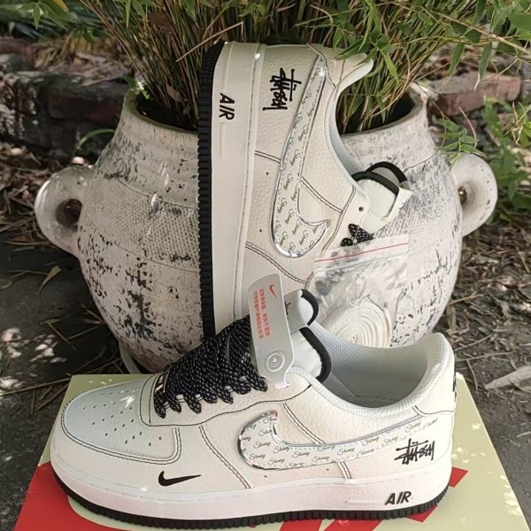 White Nike Air Force 1 sneakers with Stussy branding resting on a pale shoebox beside a potted plant.