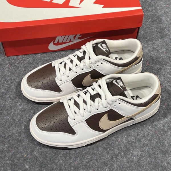 Pair of white and brown Nike sneakers with a brown Nike swoosh, placed next to a red Nike shoebox on a grey carpet.