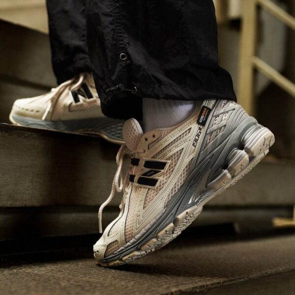White and gray running shoes with a chunky sole stepping onto a metal stair; person wearing black pants and white socks.