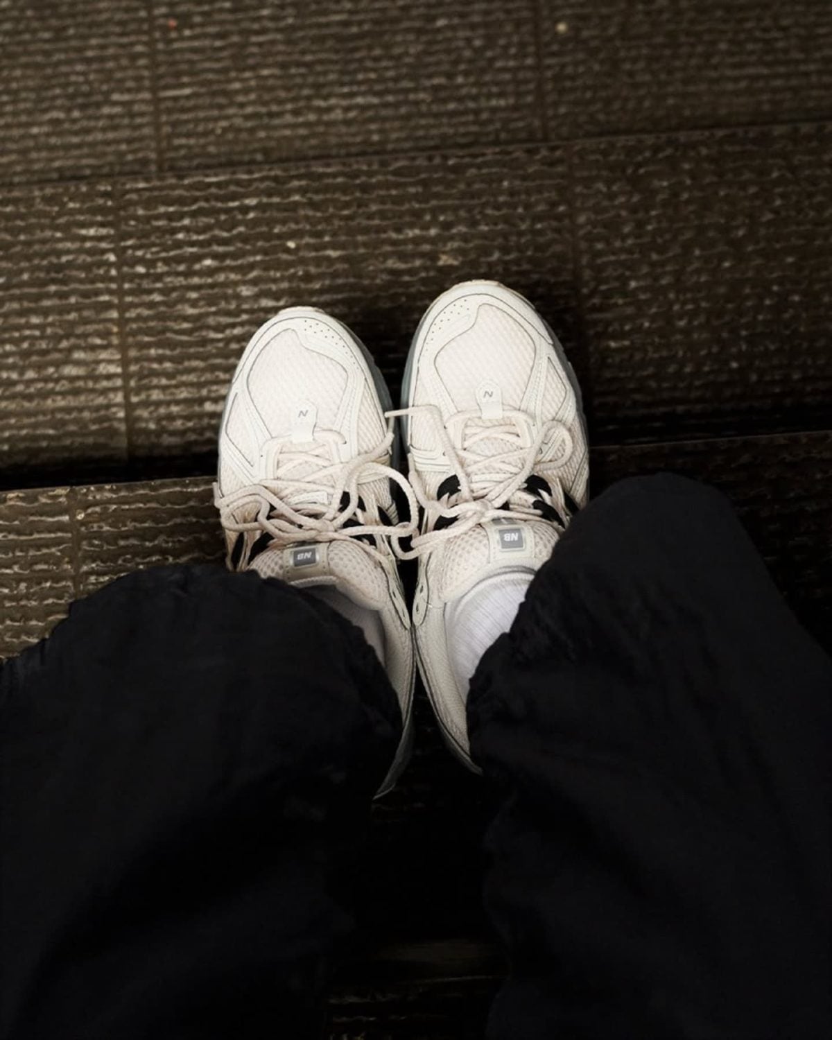 Top-down view of two white athletic sneakers on a dark wooden floor, seen from above while seated.