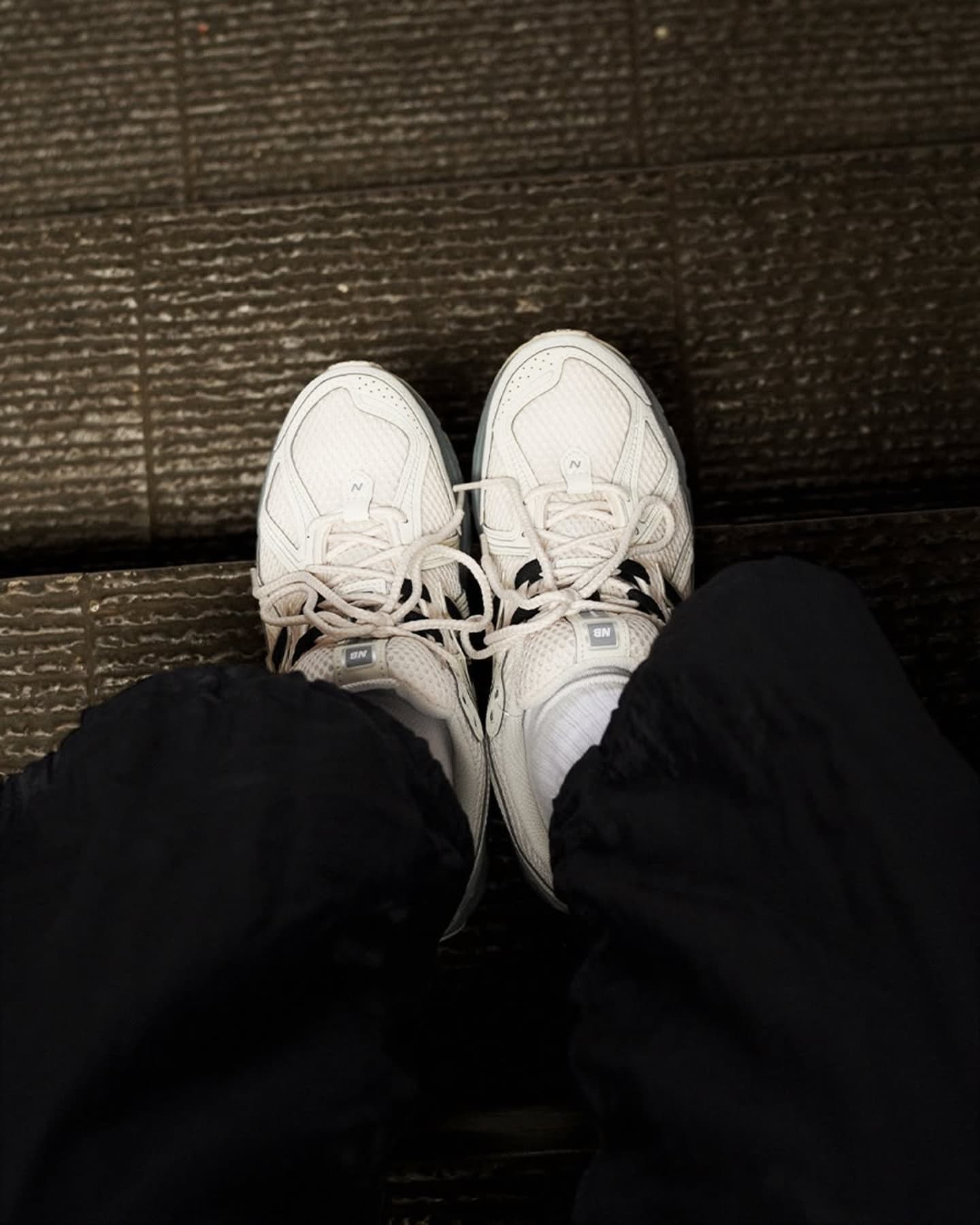 487430902_1179991066963535_5195972503864868988_n | UAE SPORT STORE Top-down view of two white athletic sneakers on a dark wooden floor, seen from above while seated.