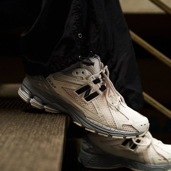 Beige New Balance running shoe on a stair step, with black pants cuffed at the ankle.