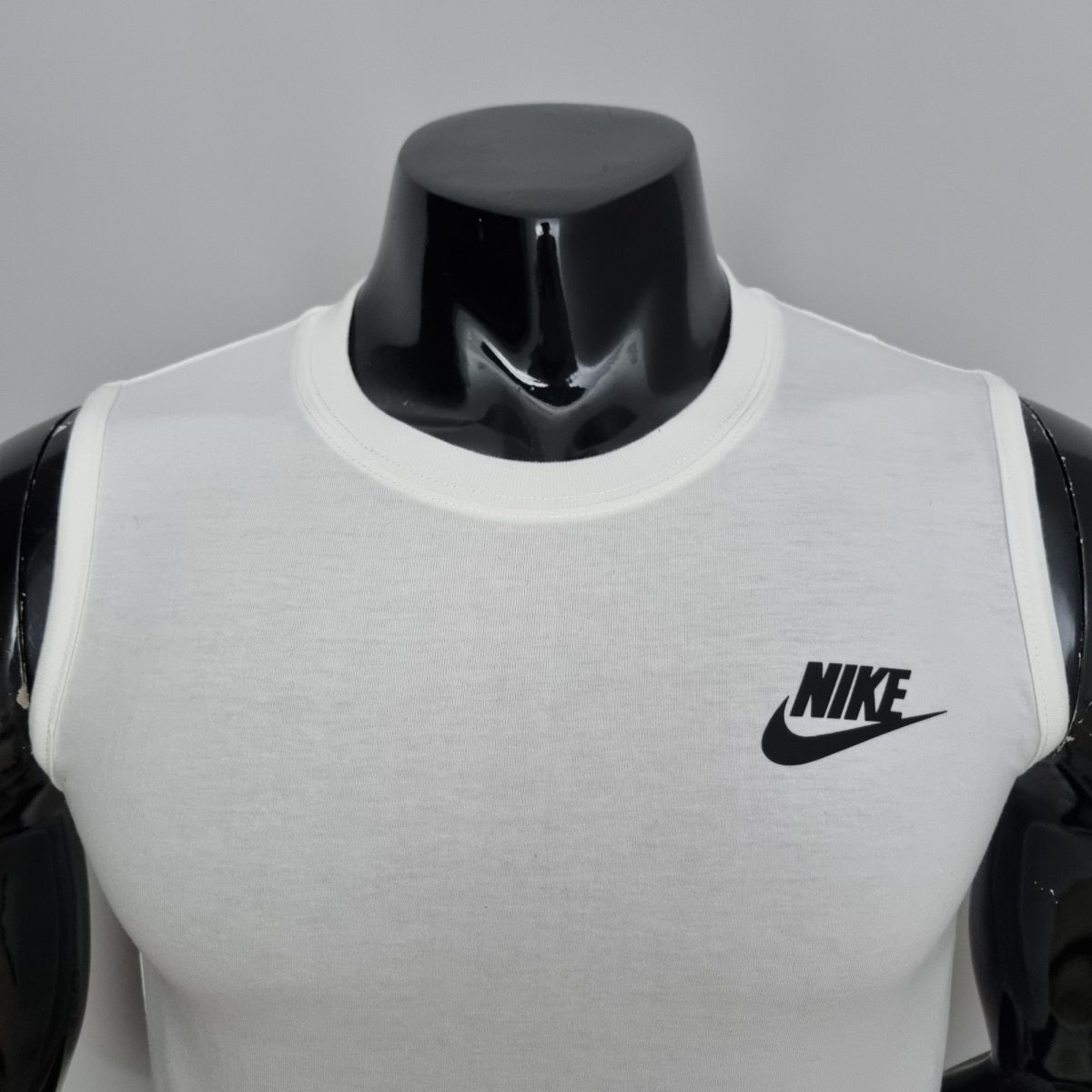 Close-up of a white Nike sleeveless shirt on a glossy black mannequin torso, with the Nike swoosh logo visible on the right chest area.
