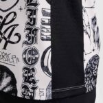 Close-up of white fabric with black graffiti-style text and graphic designs, beside a solid black panel and visible hem stitching.