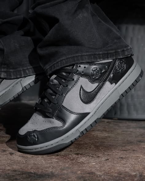 Close-up of a black and gray Nike sneaker with a visible swoosh, worn with dark jeans, on a concrete floor.