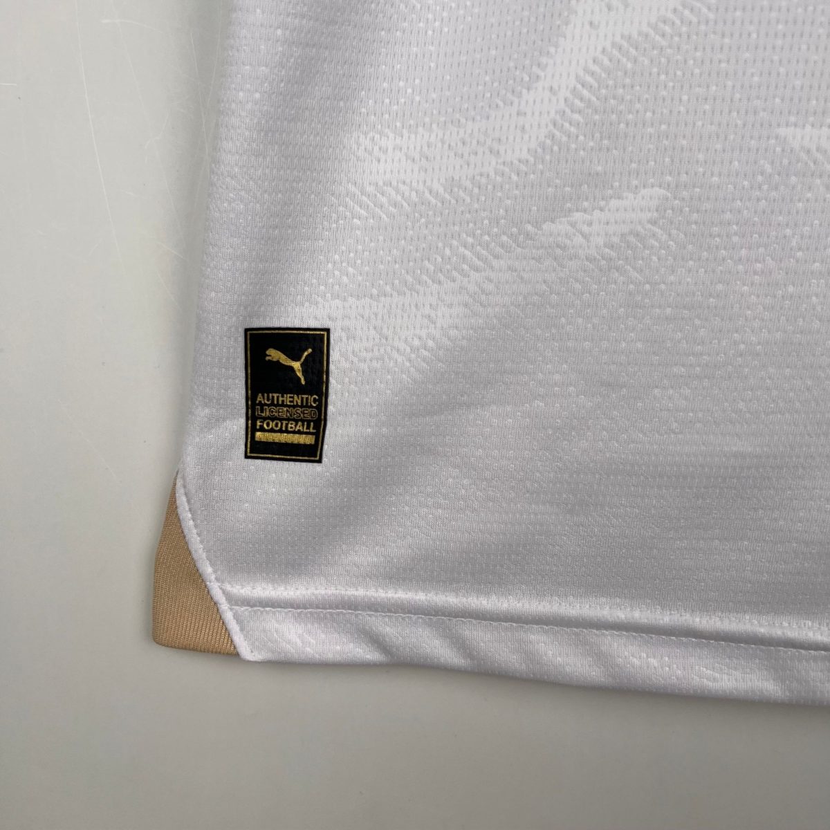 Close-up of light grey textured fabric with a small black-and-gold Puma label.