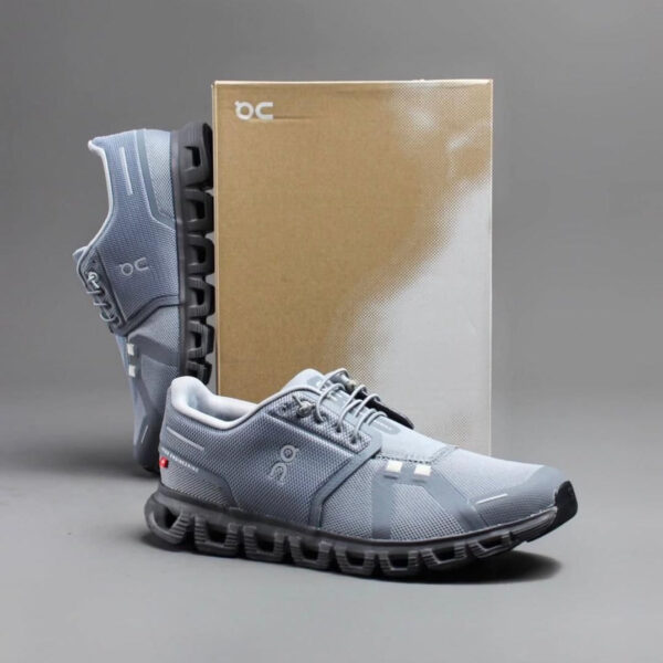 Light gray running shoes with a chunky black sole, positioned in front of a brown shoebox.
