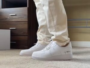 Person wearing white sneakers and beige pants standing on a carpet in a bedroom next to a wooden dresser.