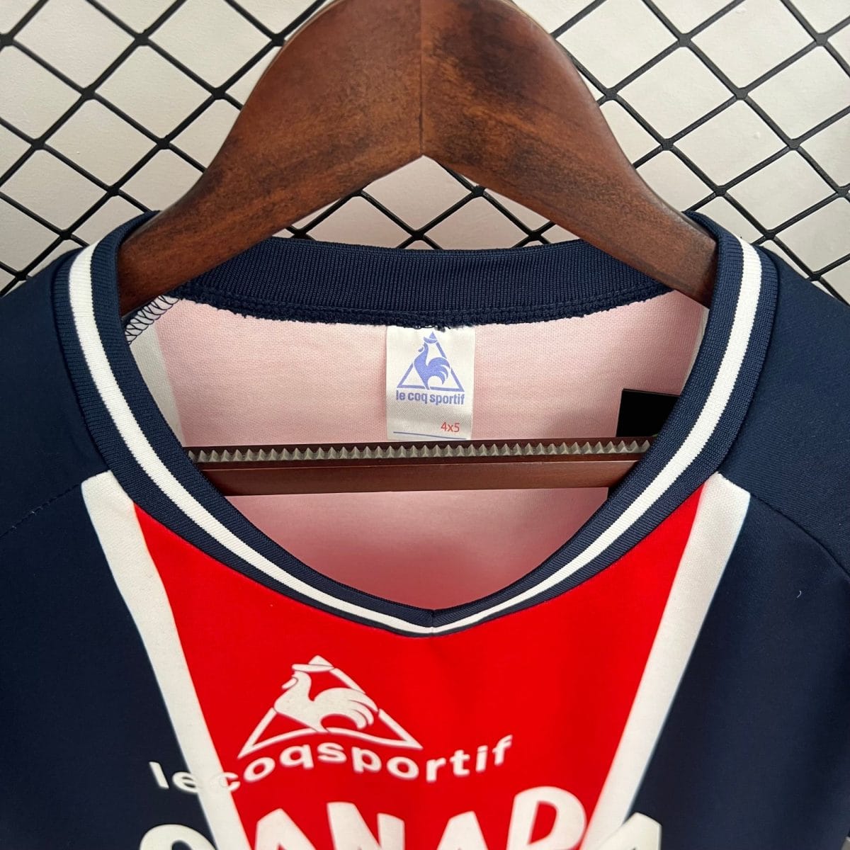 Close-up of a wooden hanger holding a pink Le Coq Sportif tag with the brand rooster logo and size 4x5.