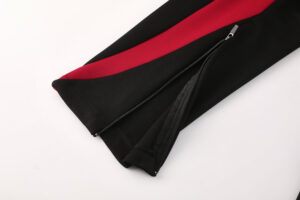 Black pants with a red side stripe and zipper pocket detail (close-up).