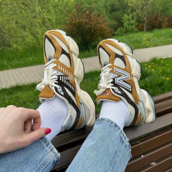 Person wearing white and tan sneakers with white socks and light-blue jeans resting their feet on a park bench, greenery in the background.