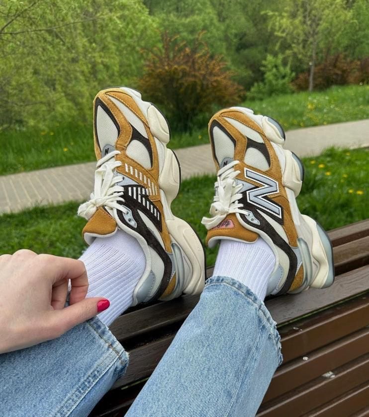 49408977-7be9-4bb4-9fbb-2a32346d077d | UAE SPORT STORE Person wearing white and tan sneakers with white socks and light-blue jeans resting their feet on a park bench, greenery in the background.
