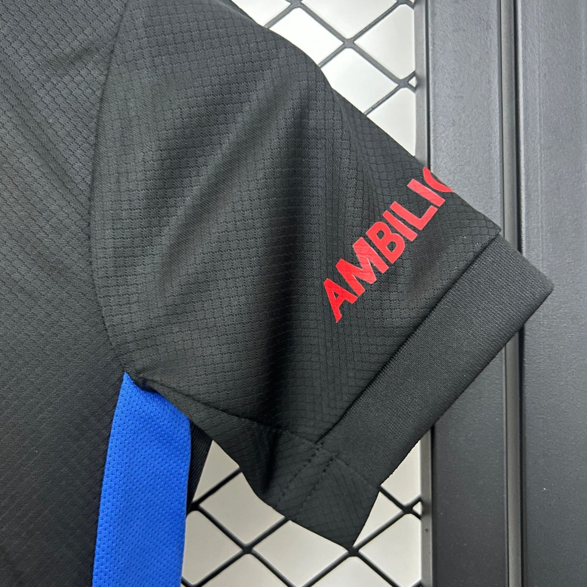 Close-up of black textured fabric with a bright blue strap and partial red lettering, against a diamond-pattern tiled background.