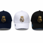 Three Real Madrid baseball caps in navy, white, and black with gold crest logos and blue trim on brims (RMCF on side).