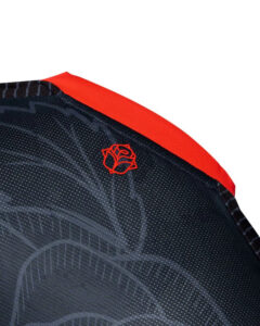 Close-up of dark fabric with a dotted texture and a small red rose emblem near a red edge seam.