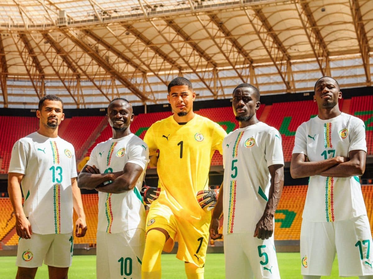 Five Senegal national team players pose for a group photo on the pitch, with the goalkeeper in yellow centered among them.