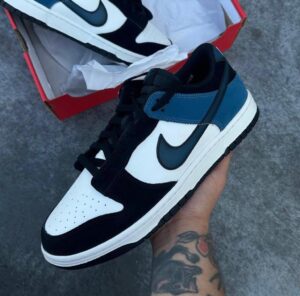Nike sneaker in white, black, and blue held in a hand with the shoebox visible in the background on a concrete surface