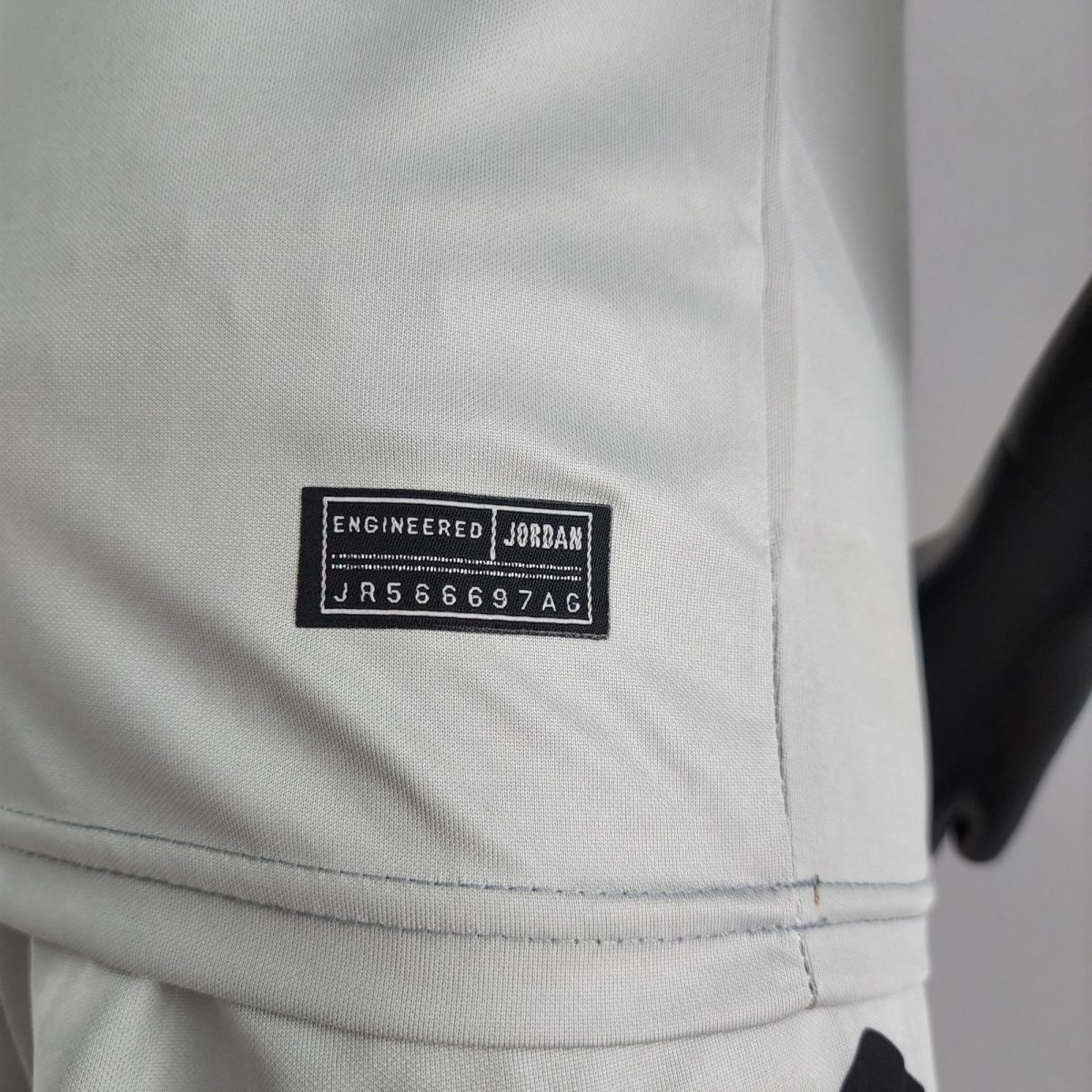 Close-up of a black fabric label sewn onto light gray textile reading 'Engineered Jordan' with a string of letters/numbers below.