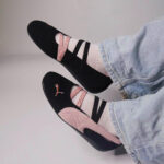 Black and pink sneakers with pink suede accents and striped straps, worn with light-pink socks and jeans. (Informative image of footwear)