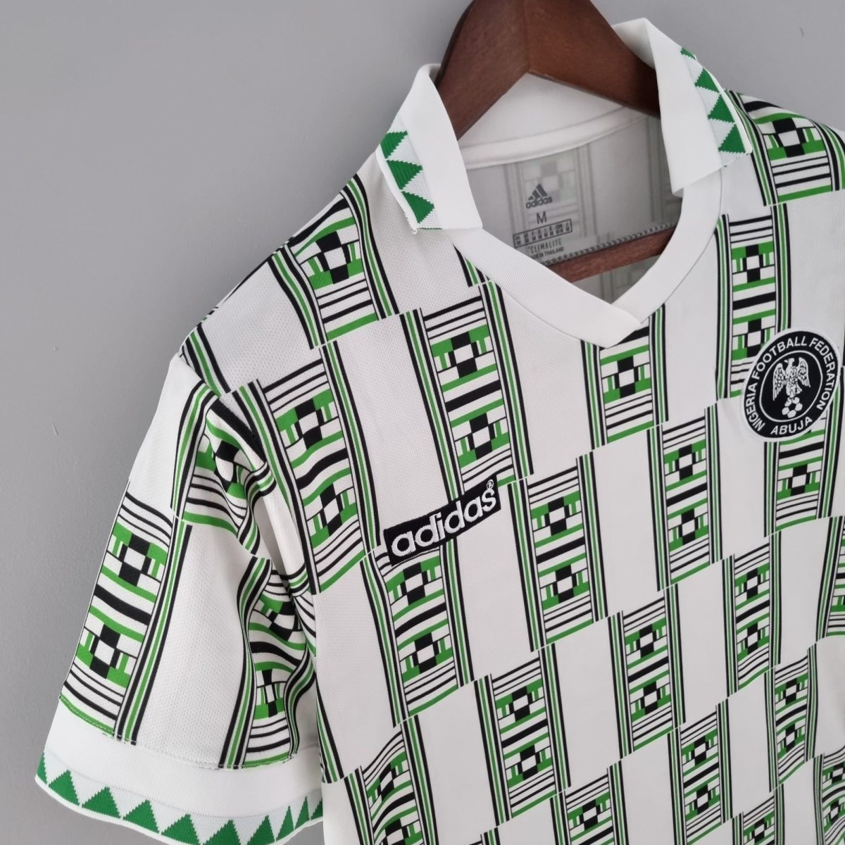 White football jersey on a hanger with green and black geometric patterns and an Adidas label visible inside the collar.