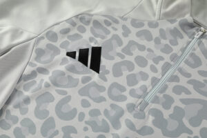 Close-up of a light gray athletic jacket with a black Adidas logo and a vertical zipper pocket.