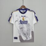 4c6323f9_592bd298-b142-4b35-a279-f81d14e245bd | UAE SPORT STORE White Real Madrid sports jersey on a wooden hanger, centered on a gray background, featuring TEKA sponsor and crest.