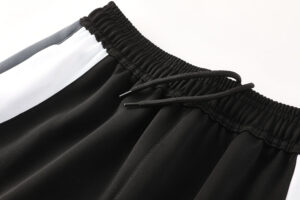 Close-up of black elastic waistband with drawstring on athletic shorts, featuring a white side stripe.