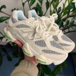 Pair of chunky white and gray sneakers with lime green accents, held up indoors against leafy background.