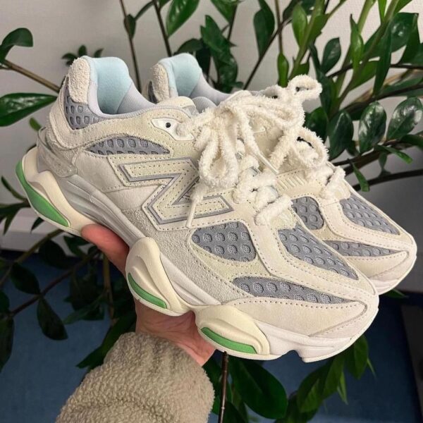 Pair of chunky white and gray sneakers with lime green accents, held up indoors against leafy background.