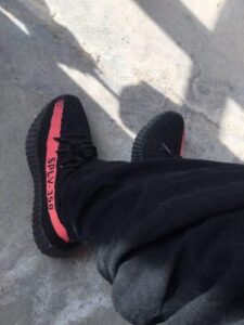 Pair of black sneakers with a pink stripe and 'SPLY-350' along the side, seen from above while standing on a concrete surface.