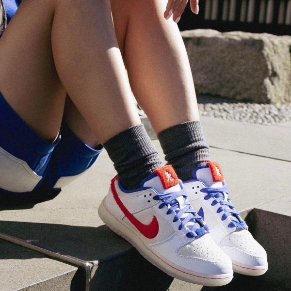 Person wearing white Nike sneakers with blue laces and an orange tongue, sitting on concrete steps with gray socks showing.