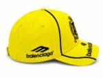 Yellow Balenciaga baseball cap with black logo and dark piping, shown from the side/forward angle.