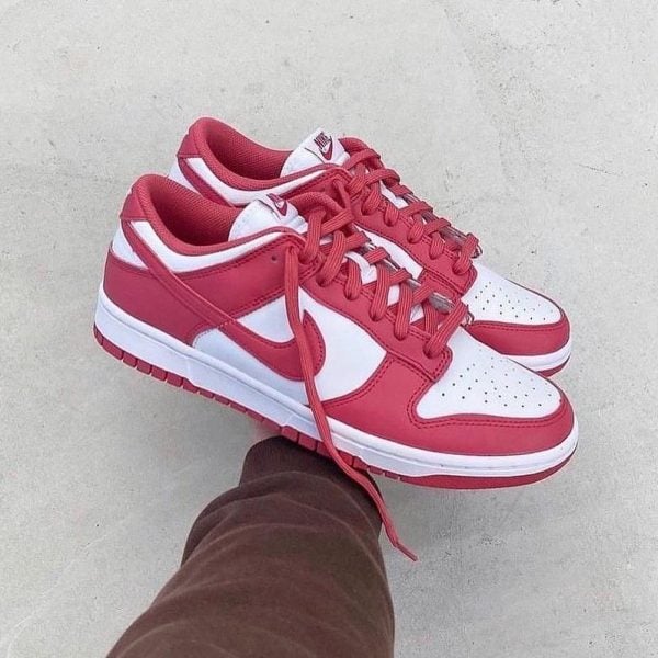 Red and white Nike sneakers being held by a person, laces loose over a gray concrete background