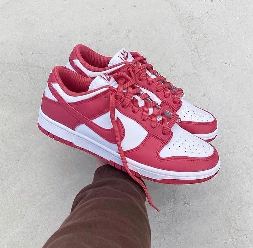 4e73d8f0-ff17-4eed-b663-9f02035a67dd | UAE SPORT STORE Red and white Nike sneakers being held by a person, laces loose over a gray concrete background