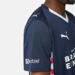 Navy Puma sports jersey with white v-neck, Puma logos on chest and shoulder, red-white side stripe, sponsor text visible on front