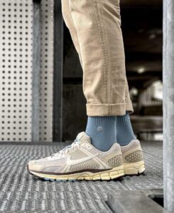 Feet wearing beige Nike running shoes, blue socks, and rolled khaki pants standing on a textured metal grate.
