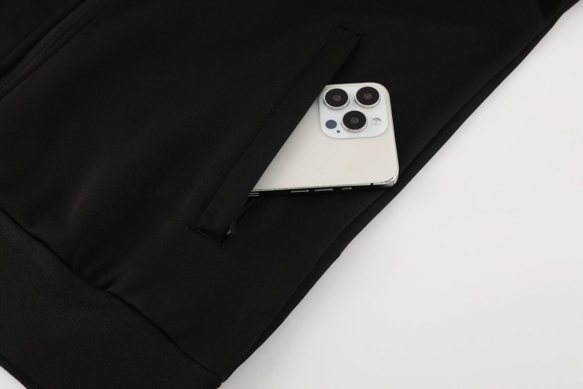 White iPhone with a triple-camera module nestled in the pocket of a black bag/backpack.