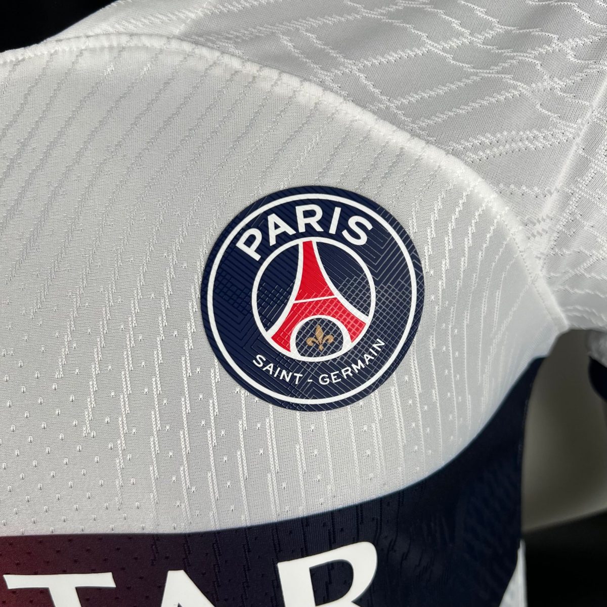 Close-up of the Paris Saint-Germain crest on quilted white fabric with a geometric pattern.