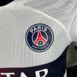 Close-up of the Paris Saint-Germain crest on quilted white fabric with a geometric pattern.