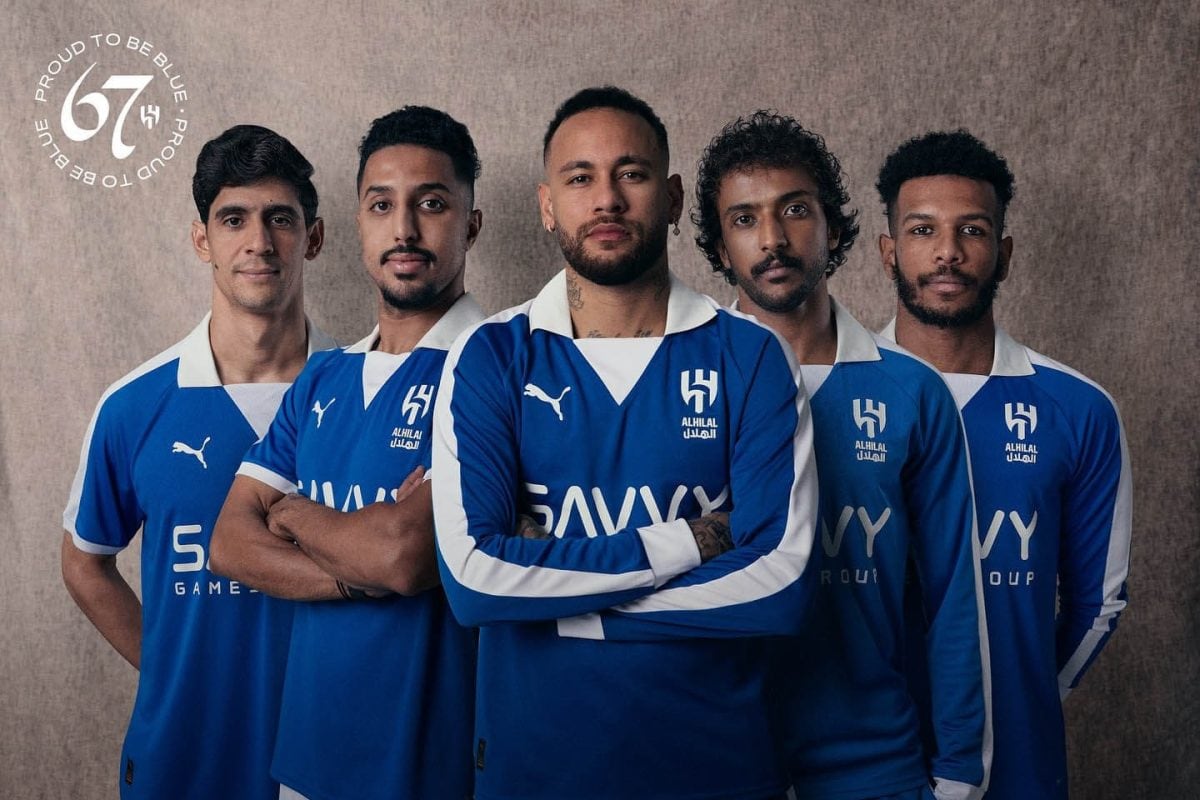 Five men in matching blue training jerseys stand together, arms crossed, facing the camera.