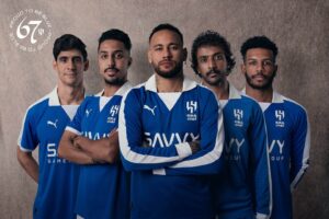 Five men in matching blue training jerseys stand together, arms crossed, facing the camera.