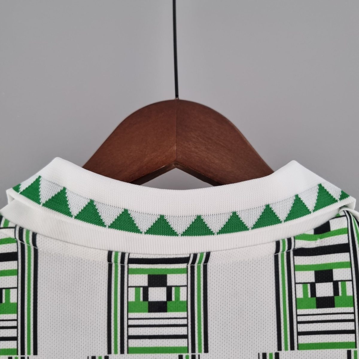 Close-up of a white shirt with a green diamond pattern on a wooden hanger against a neutral background.
