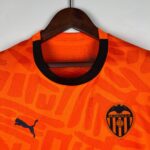 Orange Valencia CF football jersey on a hanger, showing the club crest on the chest and a black collar edge.