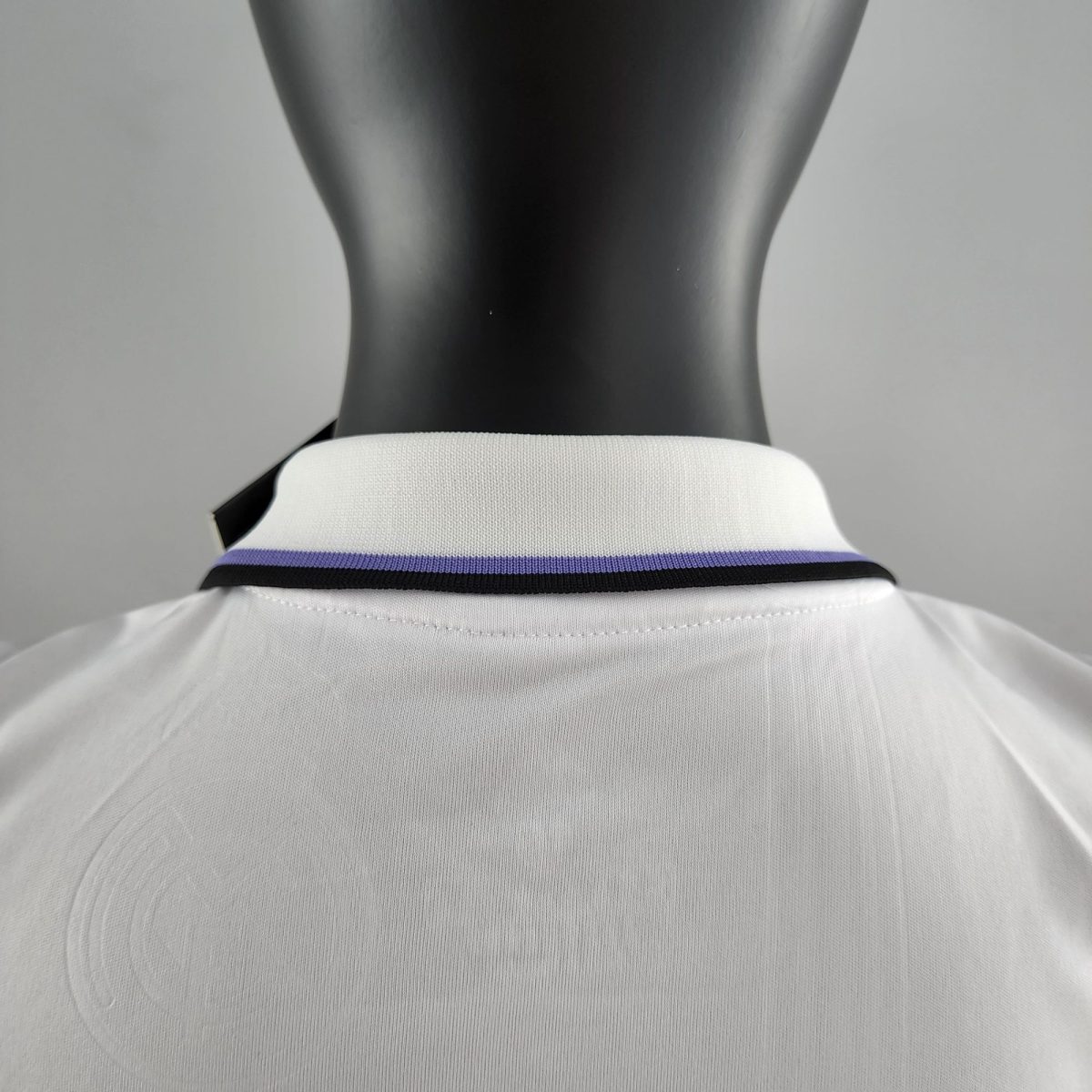 Back view of a black mannequin wearing a white polo shirt with a purple/blue striped collar viewed from behind.