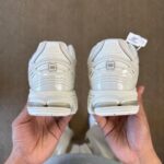 Two white sneakers held from behind, showing textured uppers, chunky heel counters, and an NB logo on each heel.