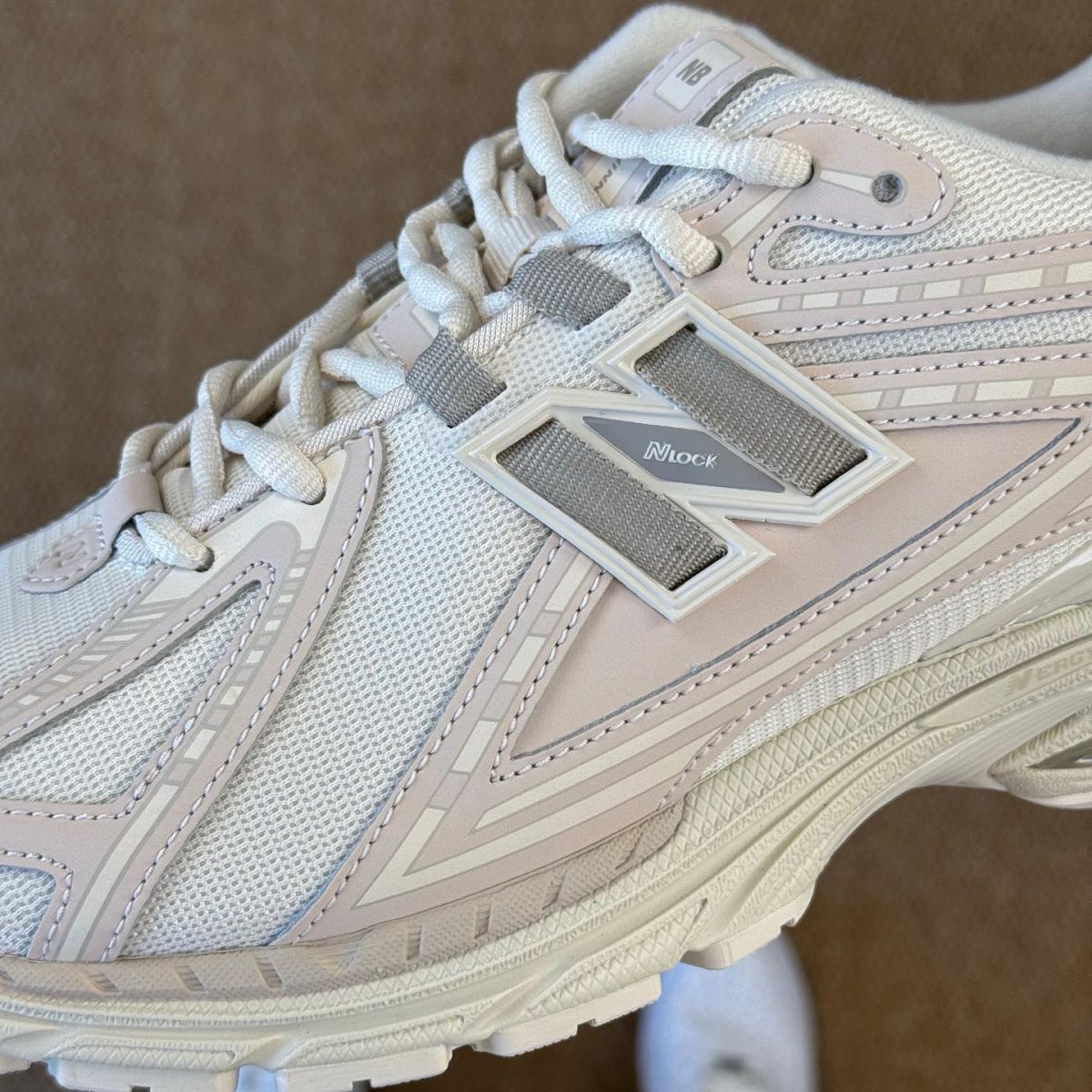 Close-up of a light gray New Balance sneaker showing mesh upper and the large 'N' logo on the side while laces are tied.