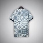 Back view of a short-sleeve shirt on a wooden hanger, featuring a blue-gray patchwork tile pattern with floral motifs and a prominent LV monogram.